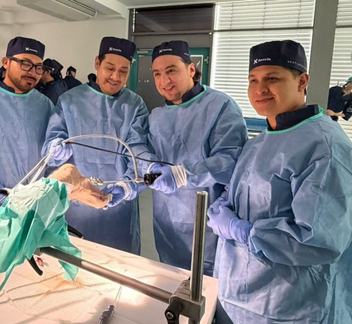 Surgical team in blue scrubs and caps perform surgery around an operating table, hands in sterile gloves.