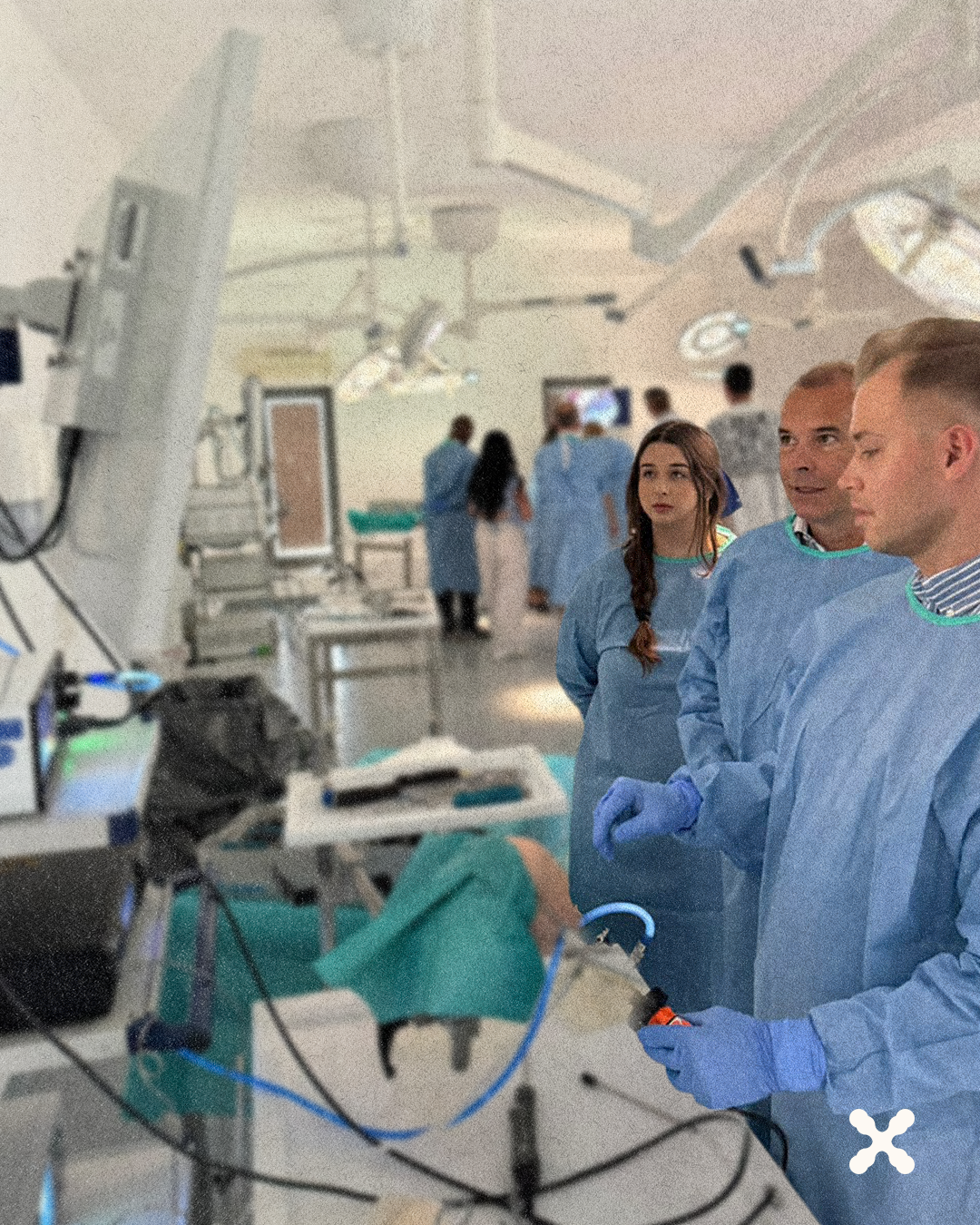 Operating room team in blue gowns and gloves gathered around an active procedure table with medical equipment nearby.