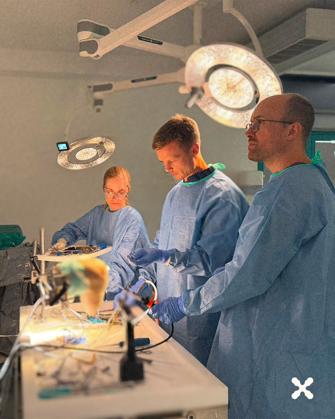 Operating room scene with surgeons in blue gowns and gloves performing surgery under bright overhead lights