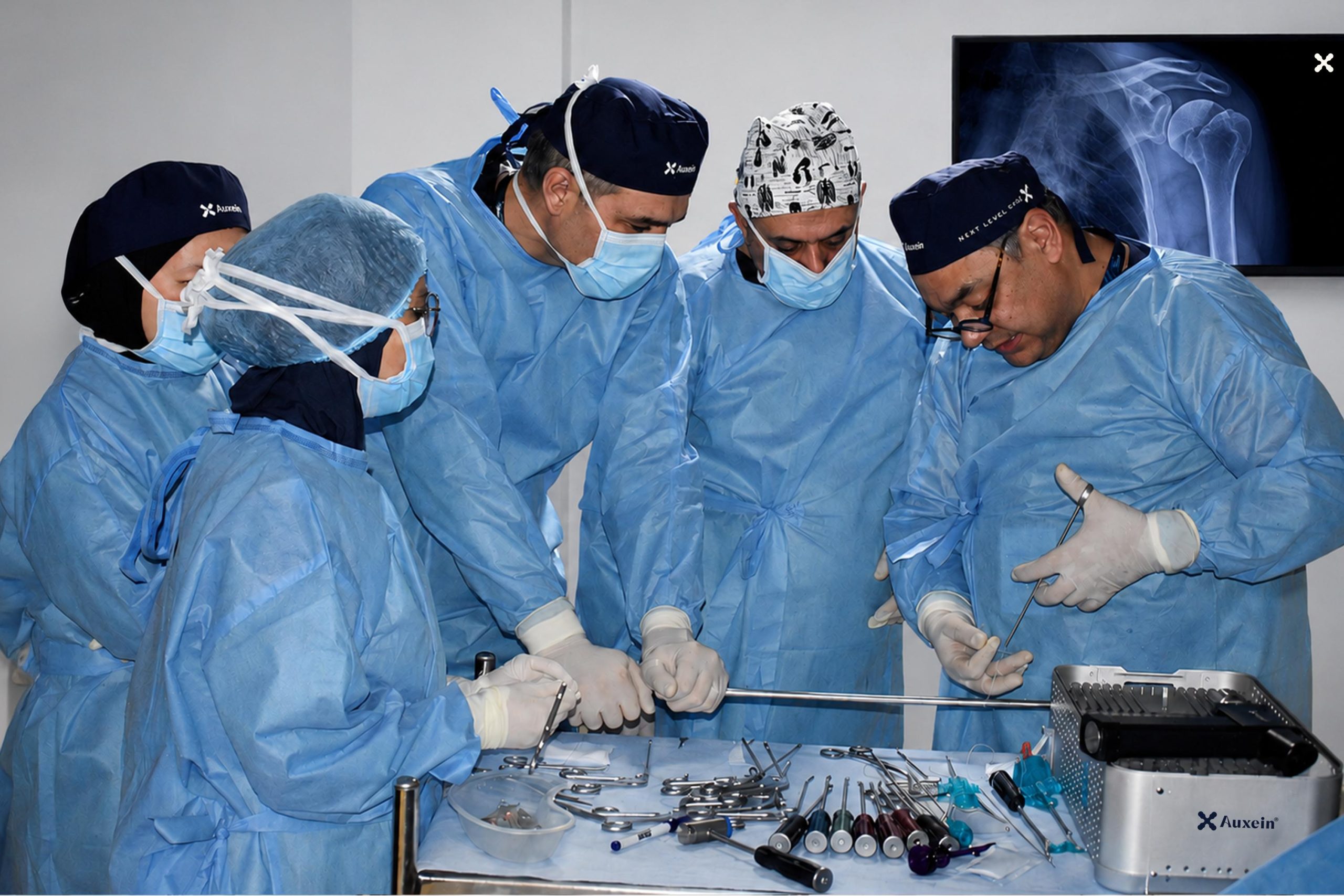 Surgeons in blue gowns and masks perform surgery around an operating table with instruments laid out nearby.