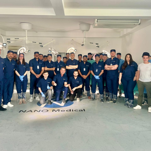 Group of medical staff in navy scrubs posing for a photo in a clinical setting, 'NANO Medical' visible on the floor.