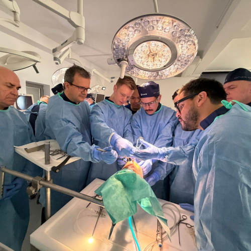 Surgical team in blue gowns and caps performing an operation under bright overhead lights in an operating room.