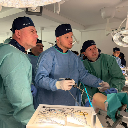 Team of surgeons in blue and green scrubs and caps performing surgery in an operating room, with a tray of instruments in the foreground.