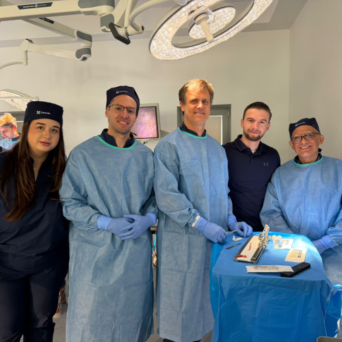 Operating room team posing for a group photo in sterile blue gowns and caps near a ready surgical tray.