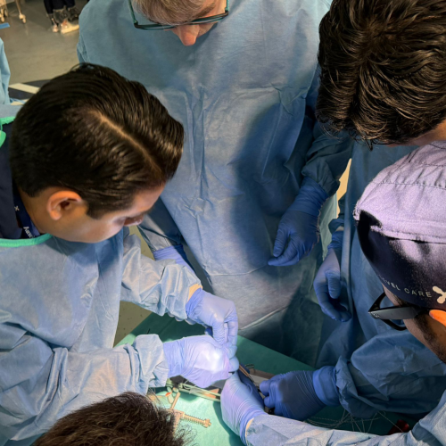 Surgeons in blue sterile gowns and gloves performing surgery, viewed from above on an operating table